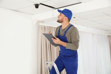 Photo of Electrician with clipboard checking camera in light room