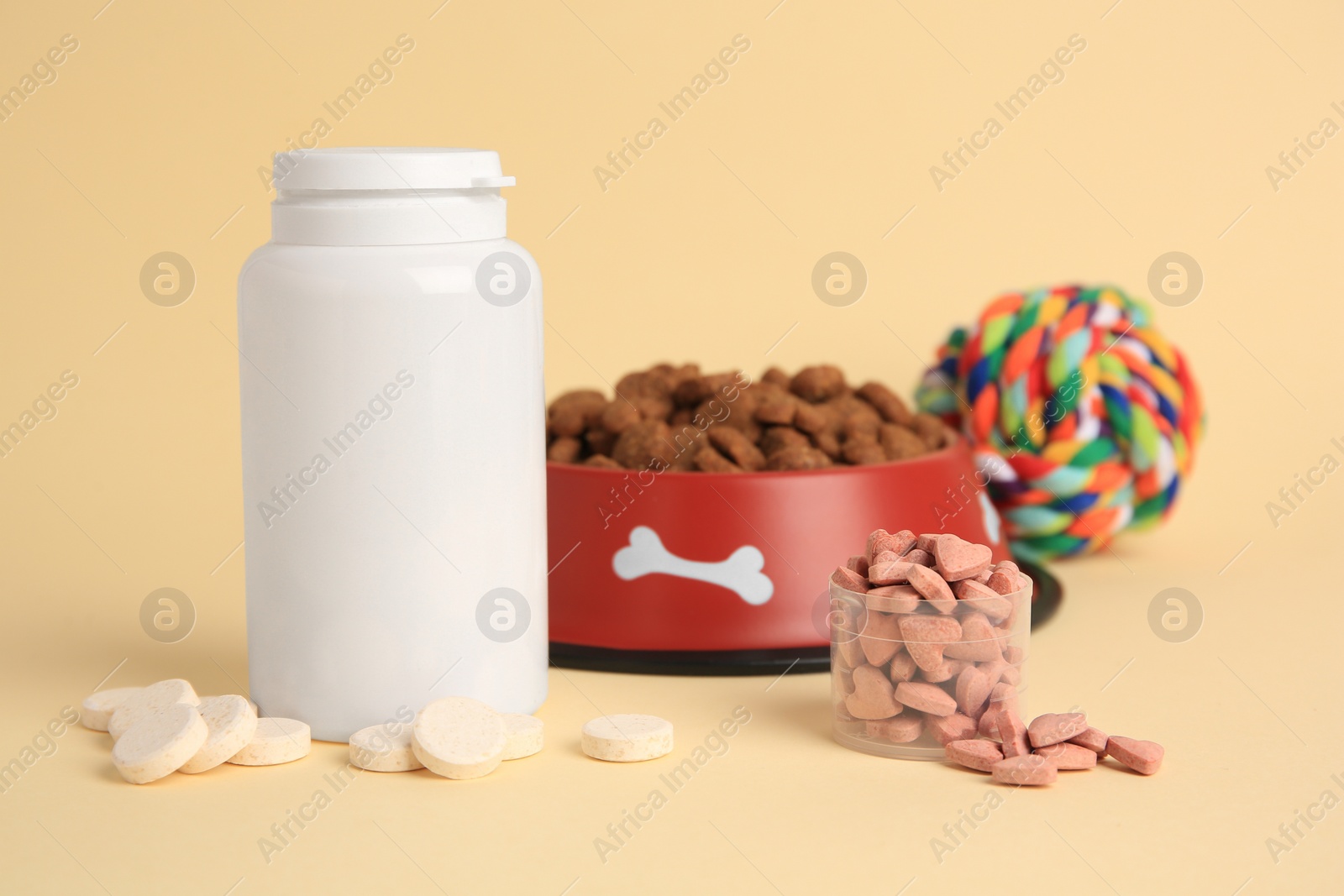 Photo of Vitamins, toy and dry pet food in bowl on beige background