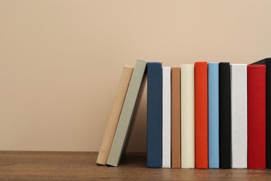Photo of Many different hardcover books on wooden table near beige wall. Space for text