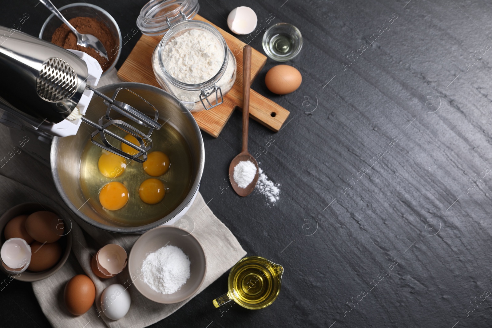 Photo of Making dough. Raw eggs in bowl of stand mixer and ingredients on black table, flat lay with space for text