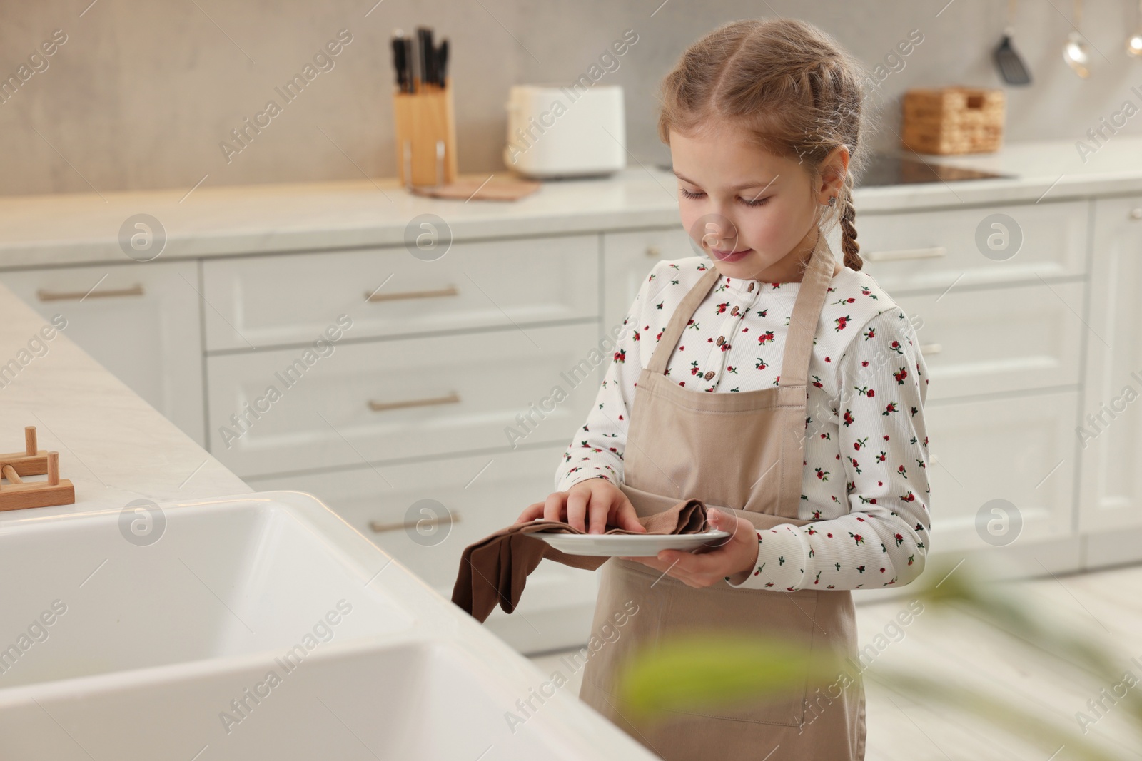 Photo of Little girl wiping plate with towel in kitchen