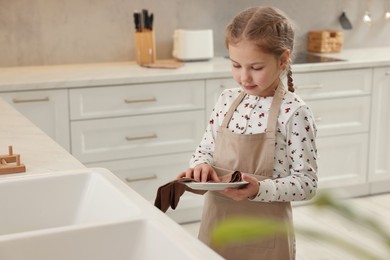 Little girl wiping plate with towel in kitchen