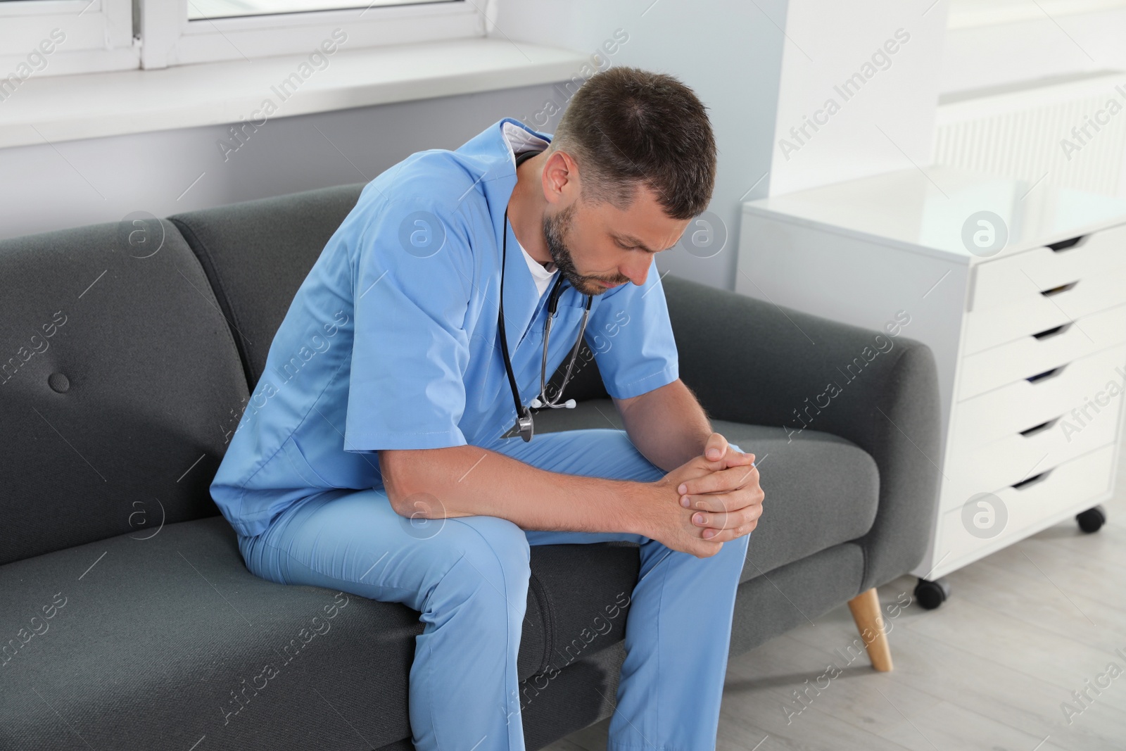 Photo of Exhausted doctor sitting on sofa in hospital