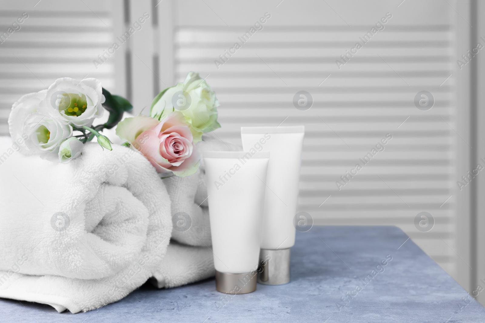 Photo of Towels, cosmetic products and flowers on grey table indoors