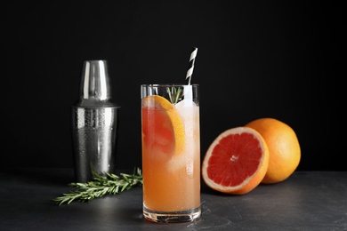 Glass of grapefruit cocktail served on table against black background