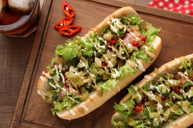 Tasty hot dogs with chili, lettuce, pickles and sauces served on wooden table, flat lay