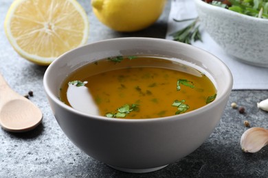 Photo of Bowl with lemon sauce on grey table, closeup. Delicious salad dressing