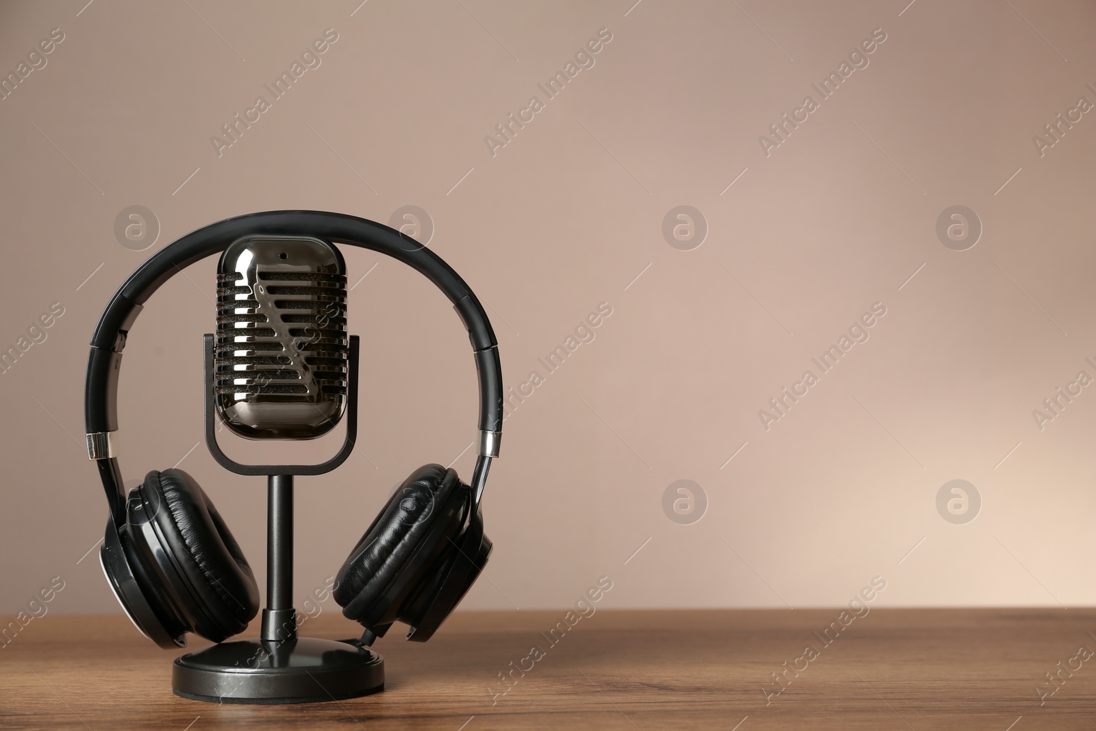 Photo of Microphone and modern headphones on wooden table against beige background, space for text