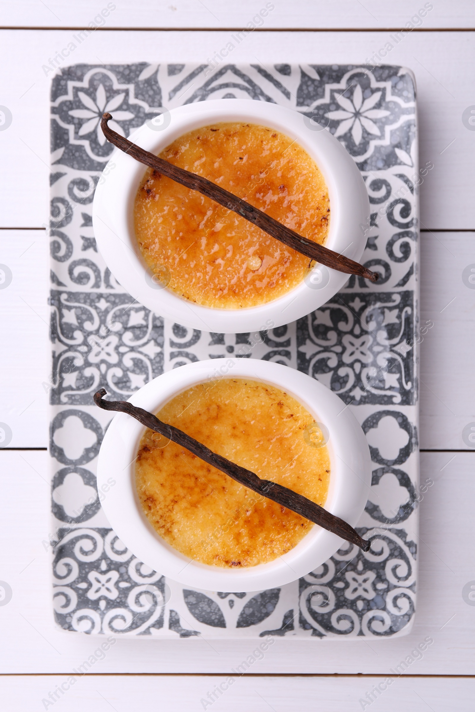 Photo of Delicious creme brulee in bowls and vanilla pods on white wooden table, top view