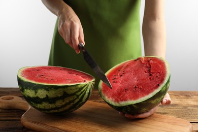 Woman cutting delicious watermelon at wooden table against light background, closeup