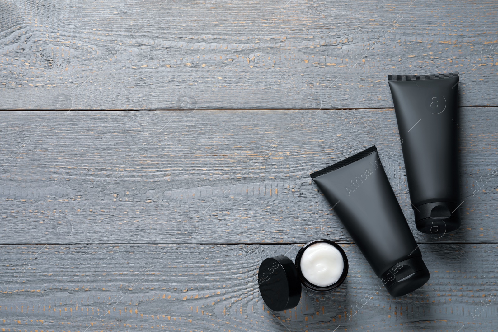 Photo of Tubes and jar with men's facial creams on grey wooden table, flat lay. Mockup for design