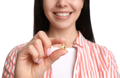 Young woman with vitamin capsule on white background, closeup