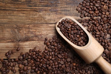 Photo of Scoop with roasted coffee beans on wooden table, flat lay. Space for text
