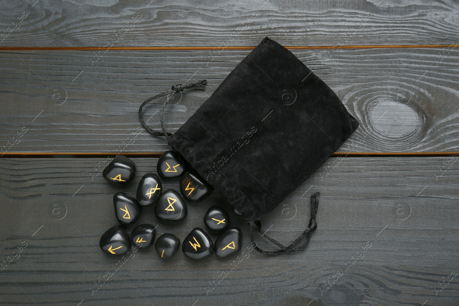 Photo of Bag with rune stones on black wooden table, flat lay