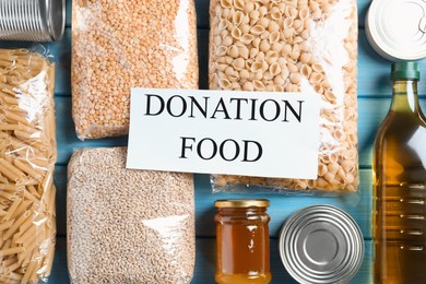 Photo of Card with words Donation Food and different products on turquoise wooden table, flat lay