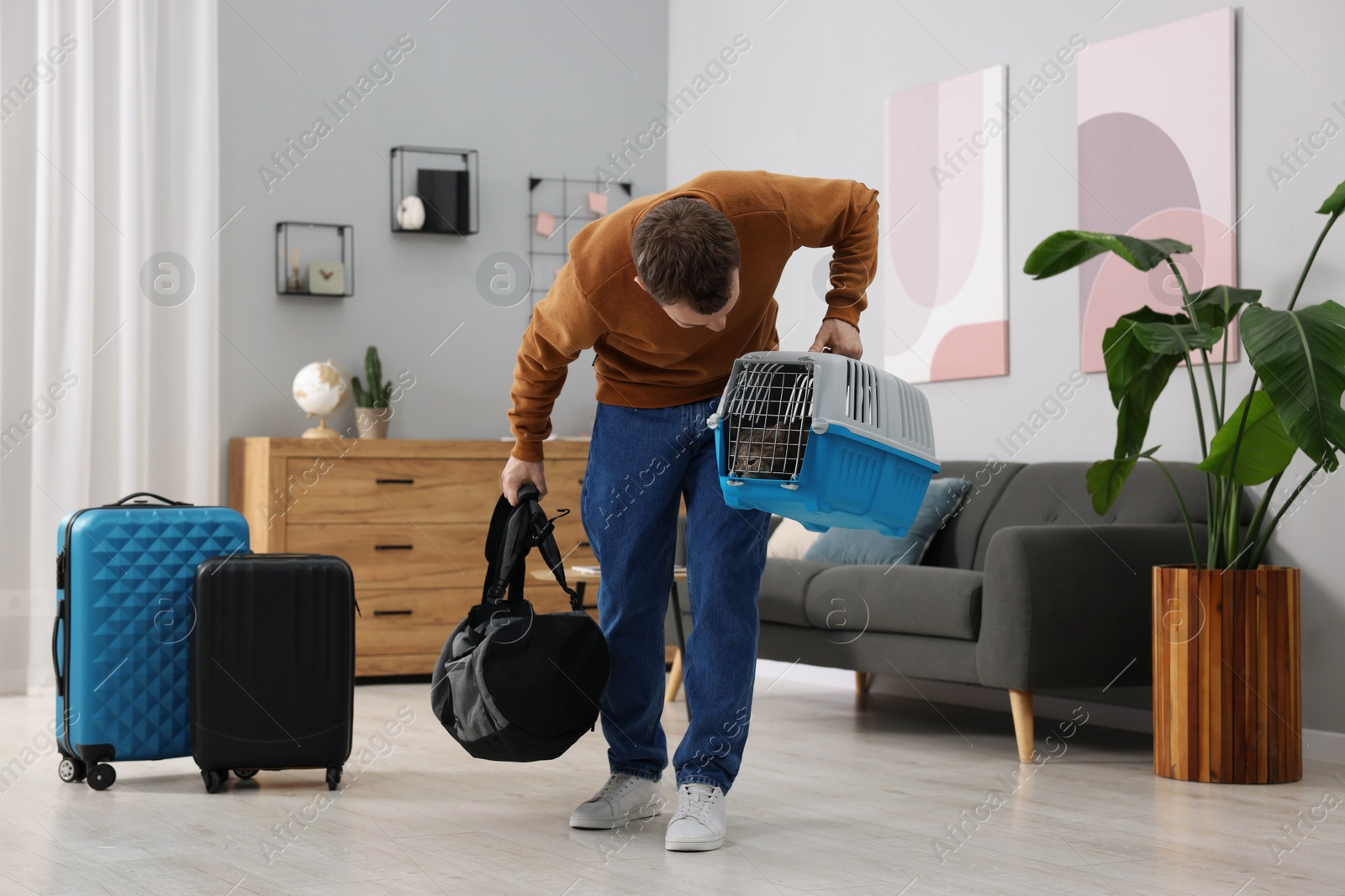 Photo of Travel with pet. Man holding carrier with cute cat and bag at home