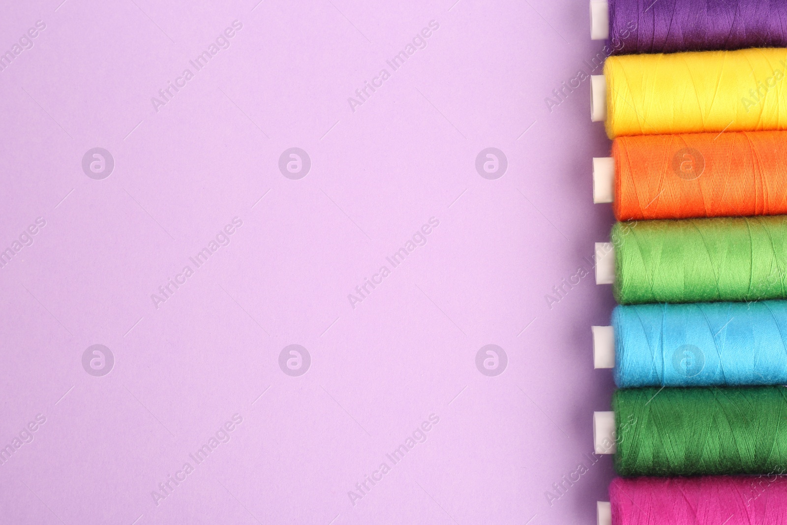 Photo of Different colorful sewing threads on lilac background, flat lay. Space for text