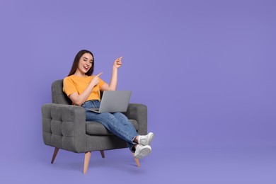 Photo of Smiling young woman with laptop sitting in armchair on lilac background, space for text