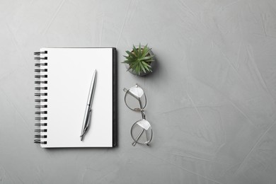 Photo of Ballpoint pen, notebook and glasses on light gray table, flat lay. Space for text