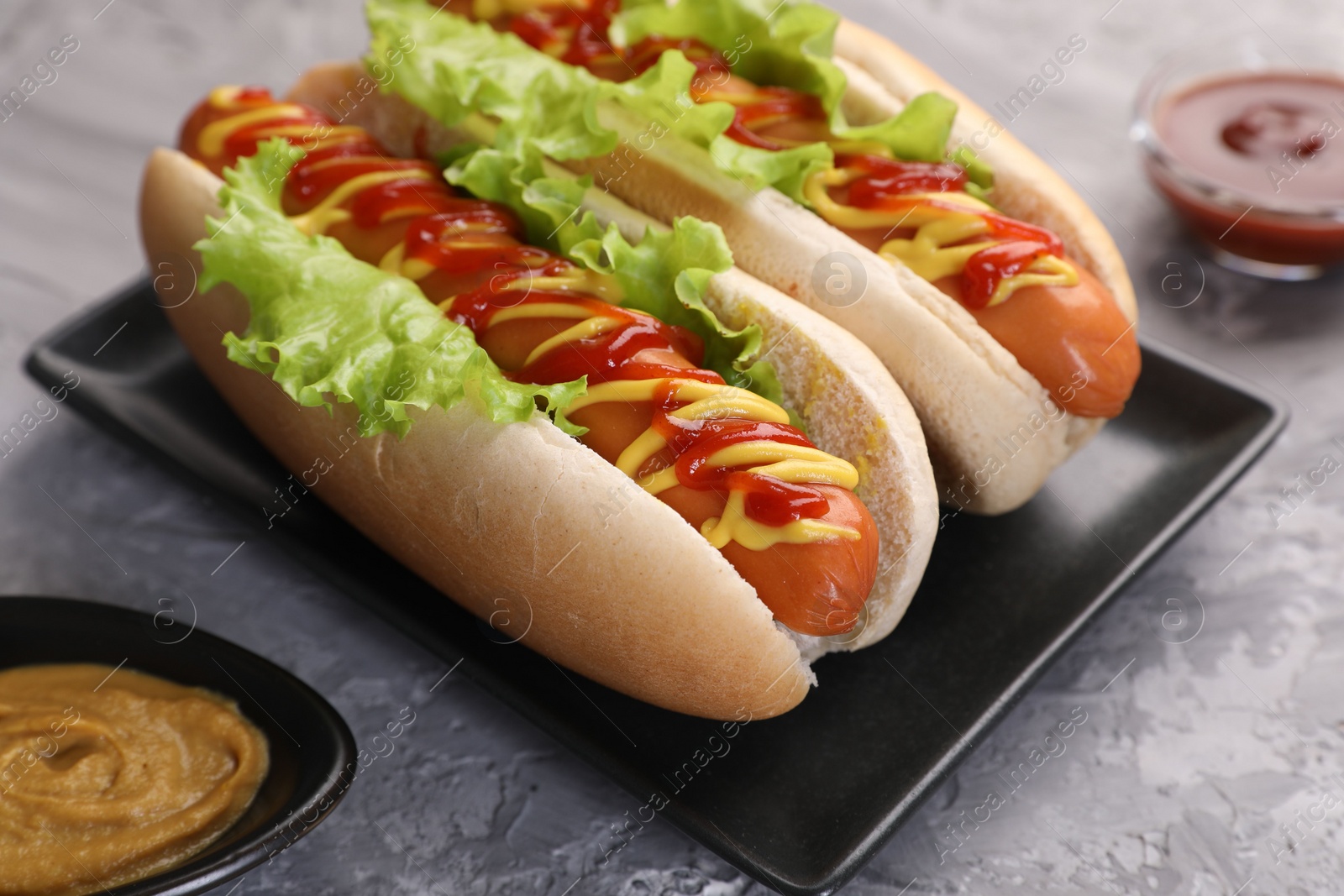 Photo of Tasty hot dogs with lettuce, ketchup and mustard on grey textured table, closeup