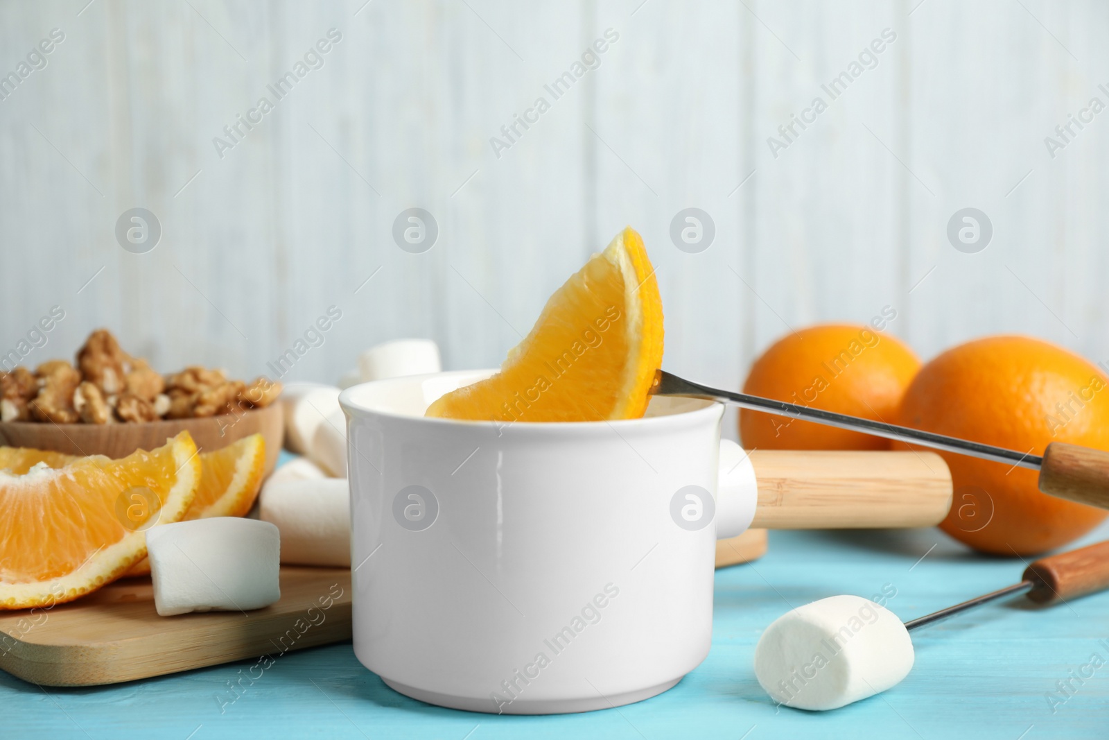 Photo of Dipping slice of orange into pot with chocolate fondue on blue wooden table