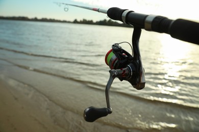 Photo of Fishing rod with reel near river, closeup. Space for text
