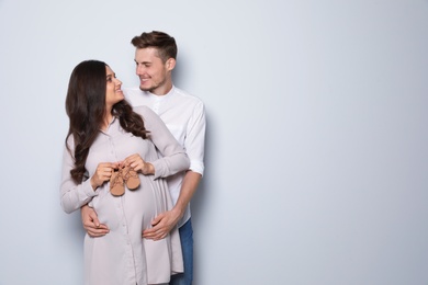 Pregnant woman and her husband holding little shoes on color background. Space for text
