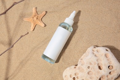 Bottle with serum, stone and starfish on sand, flat lay. Cosmetic product