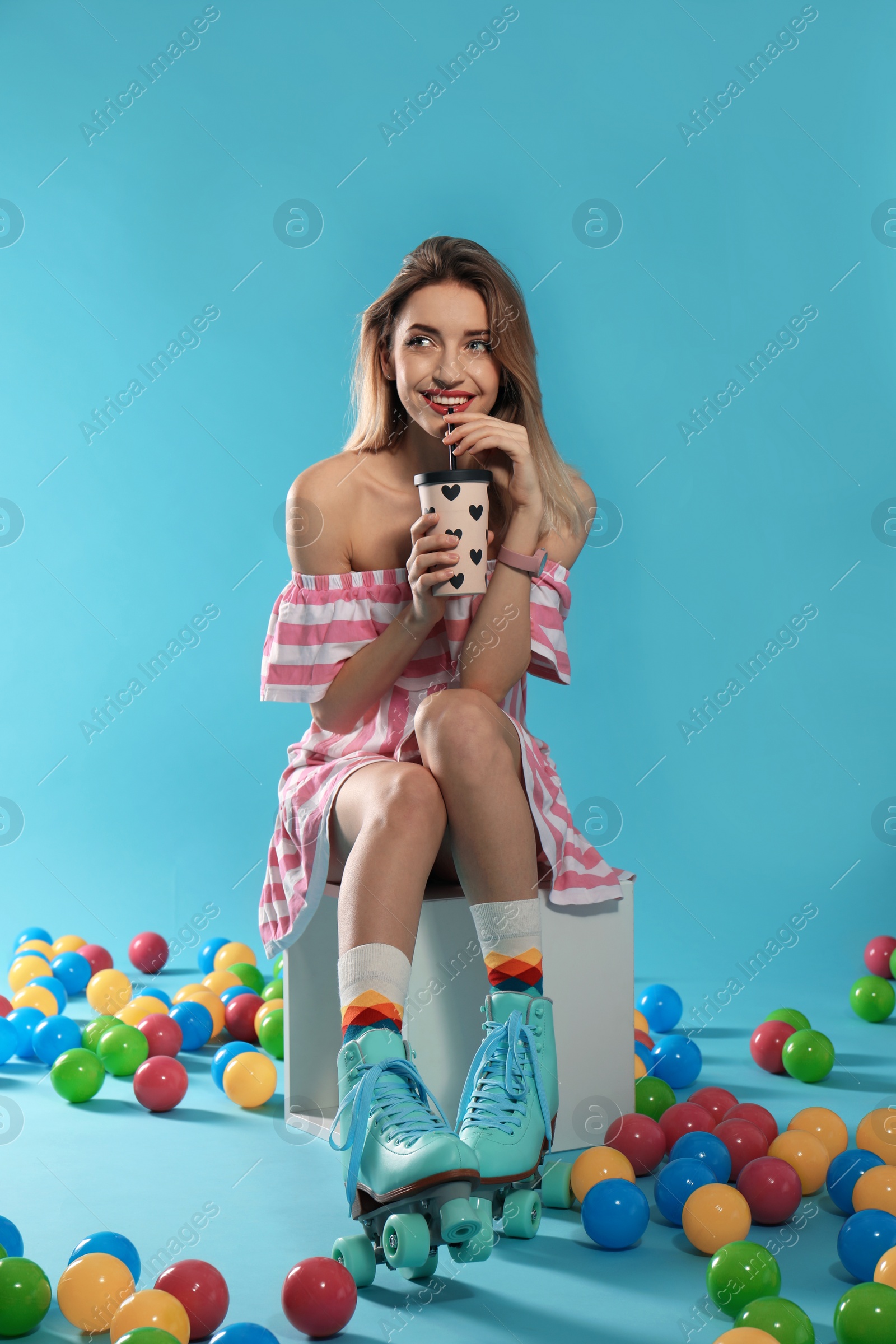 Photo of Young woman with retro roller skates and cup of drink on color background