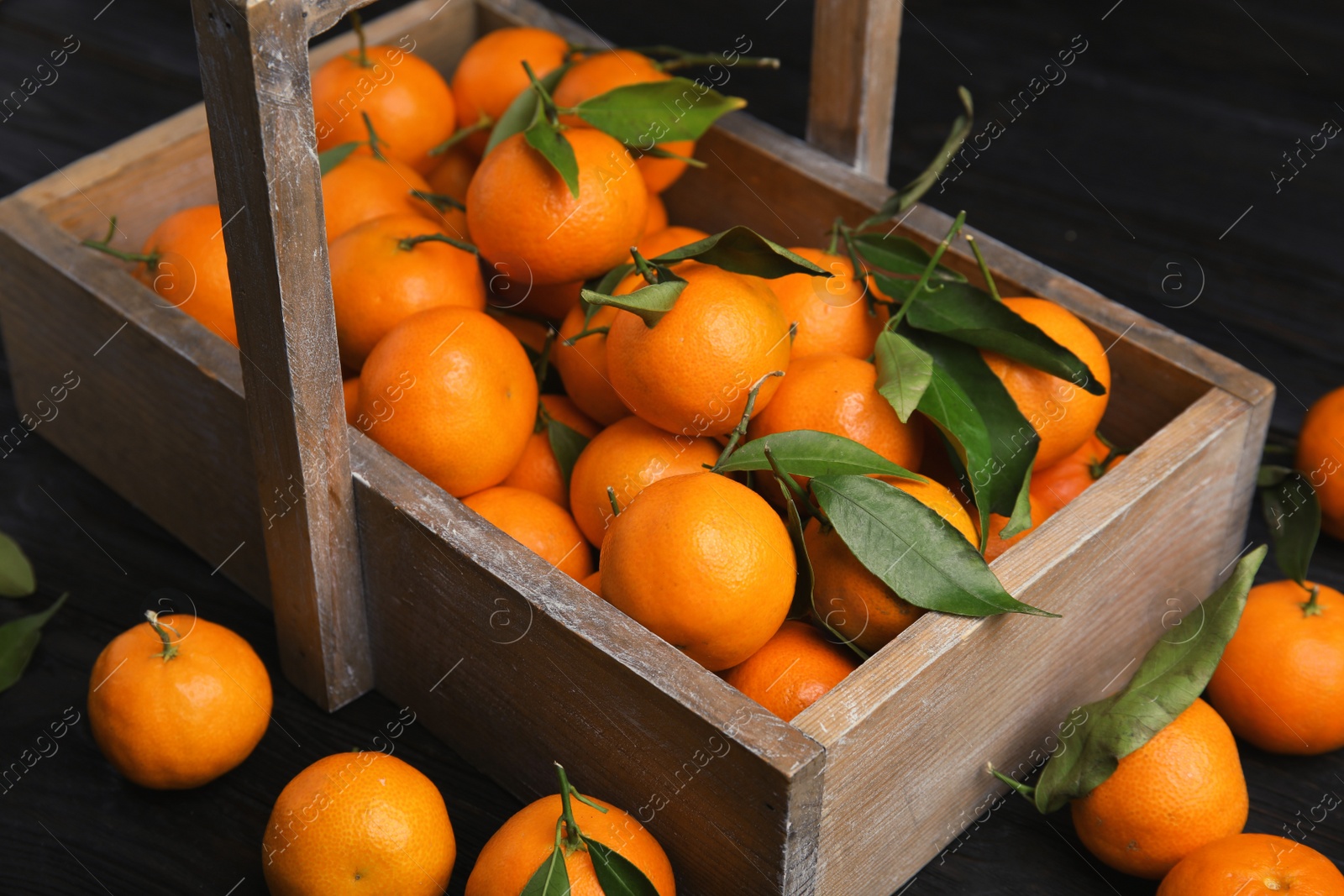 Photo of Fresh ripe tangerines with green leaves and wooden basket on table