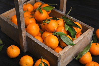 Photo of Fresh ripe tangerines with green leaves and wooden basket on table