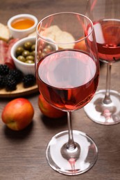 Photo of Delicious rose wine and snacks on wooden table, closeup