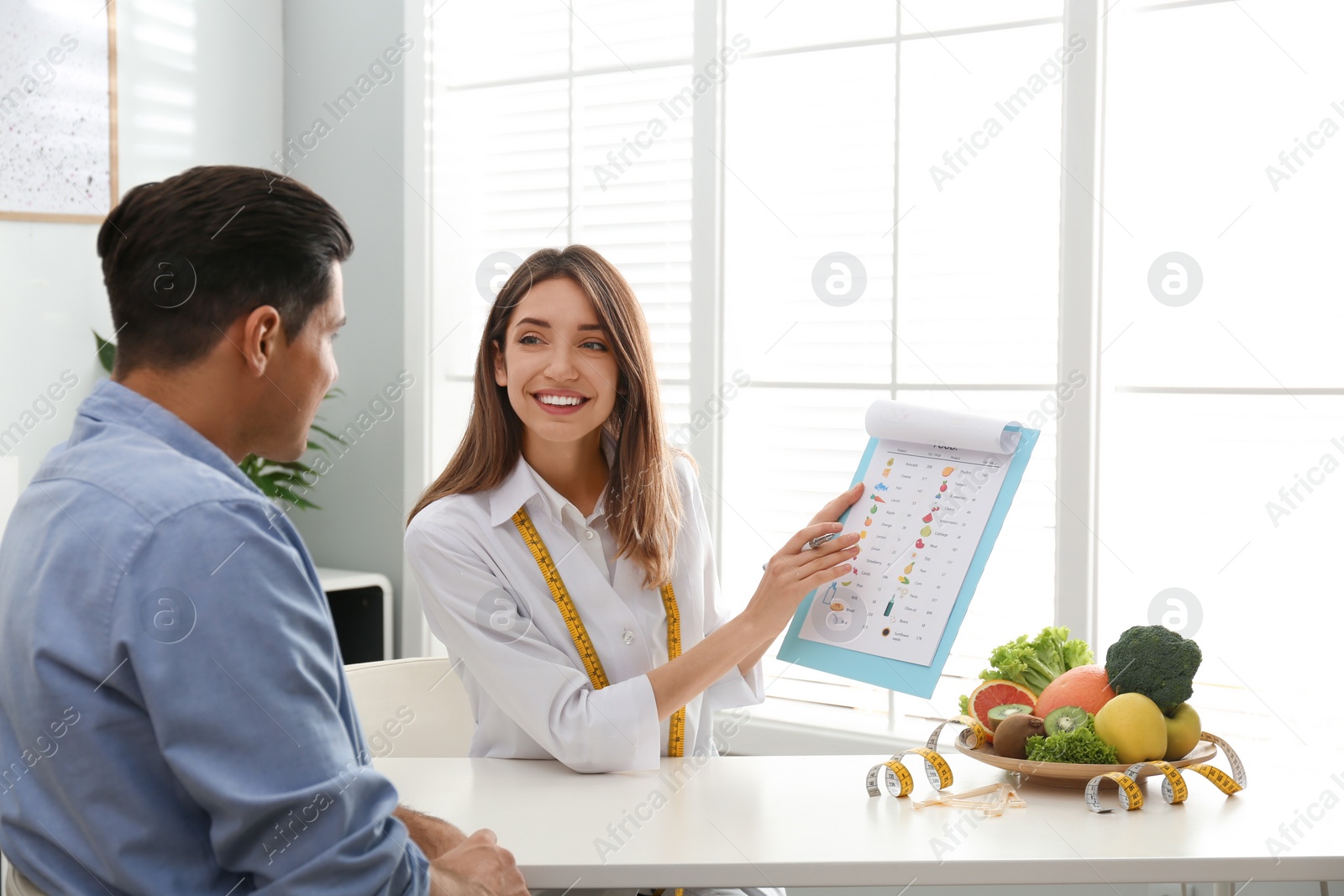 Photo of Young nutritionist consulting patient at table in clinic