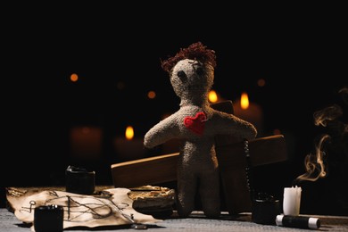 Photo of Voodoo doll with pin in heart and ceremonial items on wooden table against blurred background