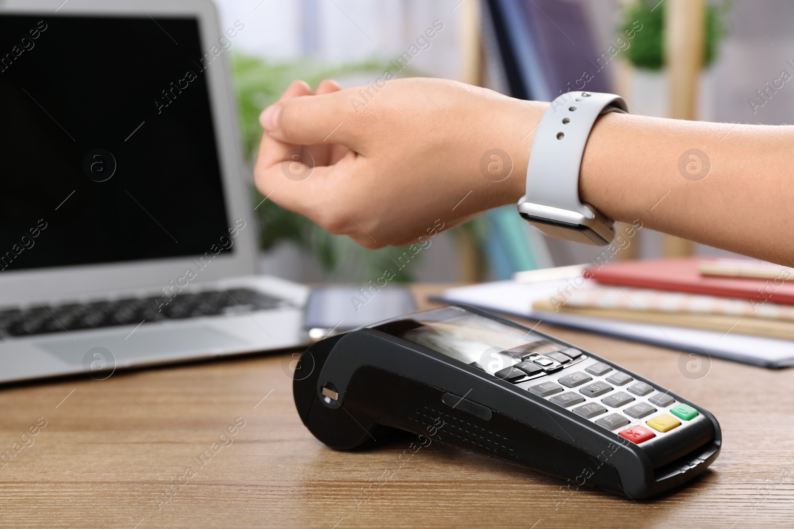 Photo of Woman using terminal for contactless payment with smart watch at table