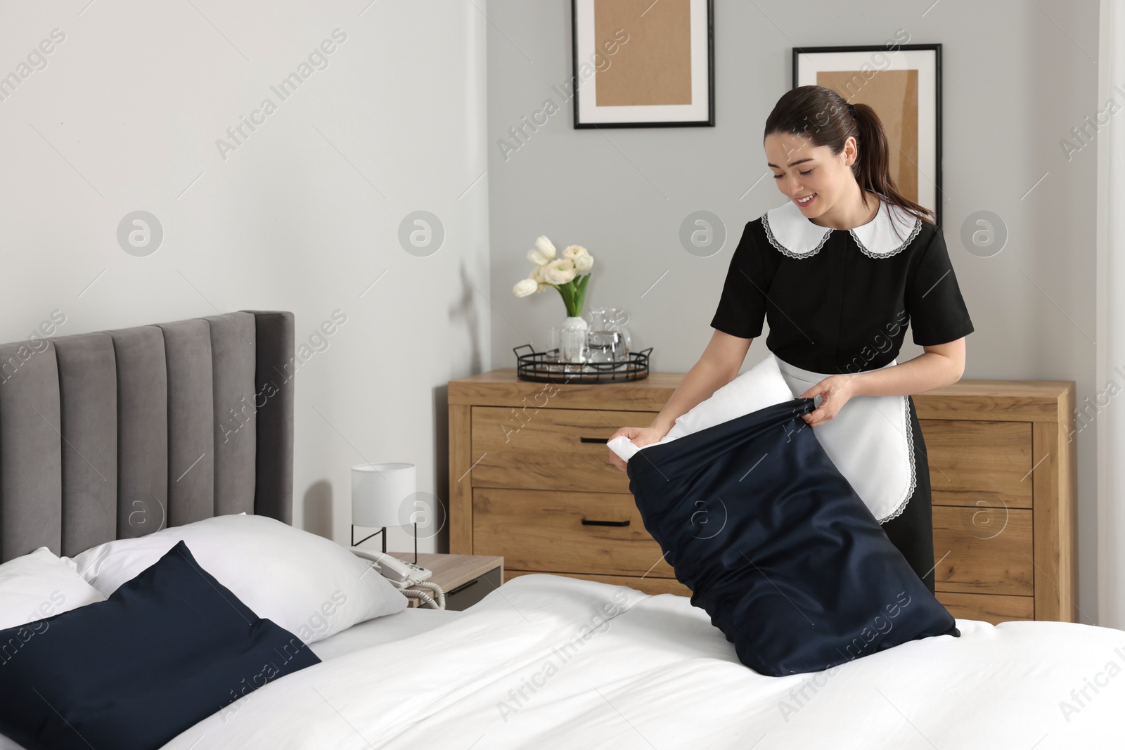 Photo of Young chambermaid making bed in hotel room