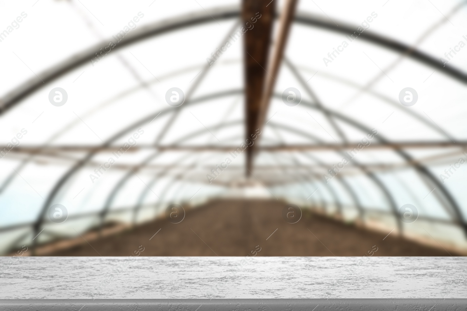 Image of Empty stone surface and blurred view of large agricultural greenhouse. Space for text