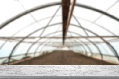 Empty stone surface and blurred view of large agricultural greenhouse. Space for text