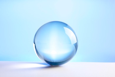 Photo of Transparent glass ball on table against light blue background