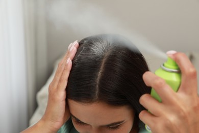 Photo of Woman applying dry shampoo onto her hair, closeup