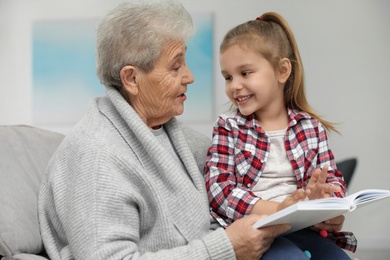 Photo of Cute girl and her grandmother reading book at home