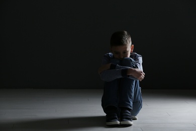 Upset boy sitting in dark room. Space for text