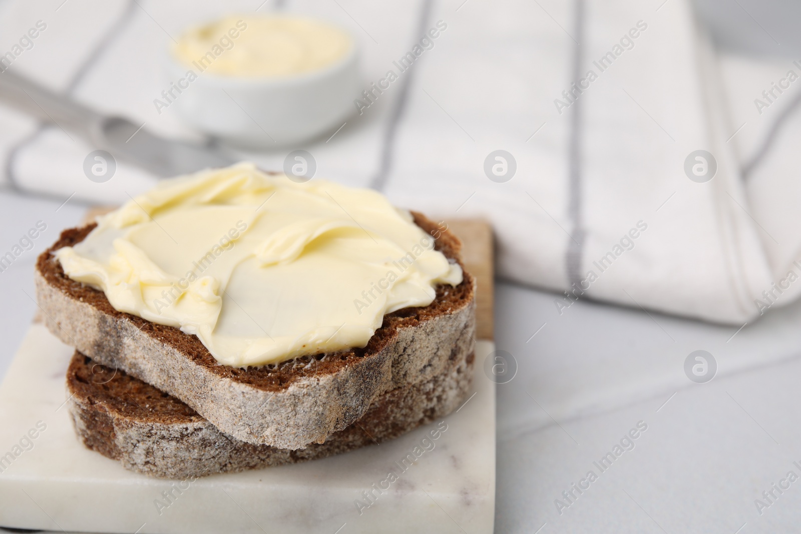 Photo of Slices of tasty bread with butter on white tiled table, closeup. Space for text