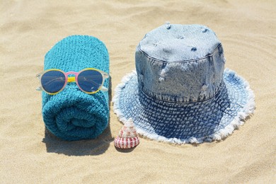 Photo of Towel with sunglasses, seashell and denim hat on sand outdoors. Beach accessories