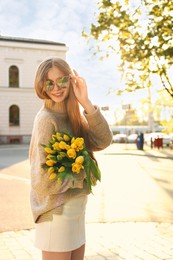 Photo of Beautiful teenage girl with bouquet of yellow tulips on city street