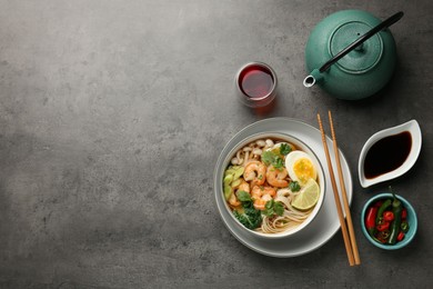 Photo of Delicious ramen with shrimps in bowl served on grey table, flat lay with space for text. Noodle soup