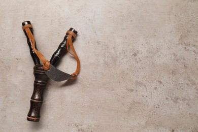 Photo of Black slingshot with leather pouch on light grey table, top view. Space for text