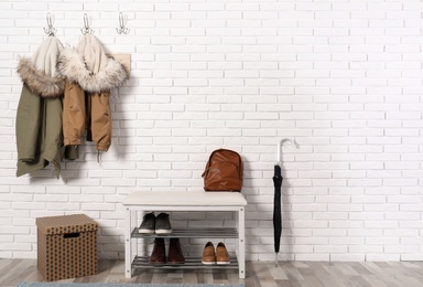 Photo of Stylish hallway interior with shoe rack and hanging clothes on brick wall