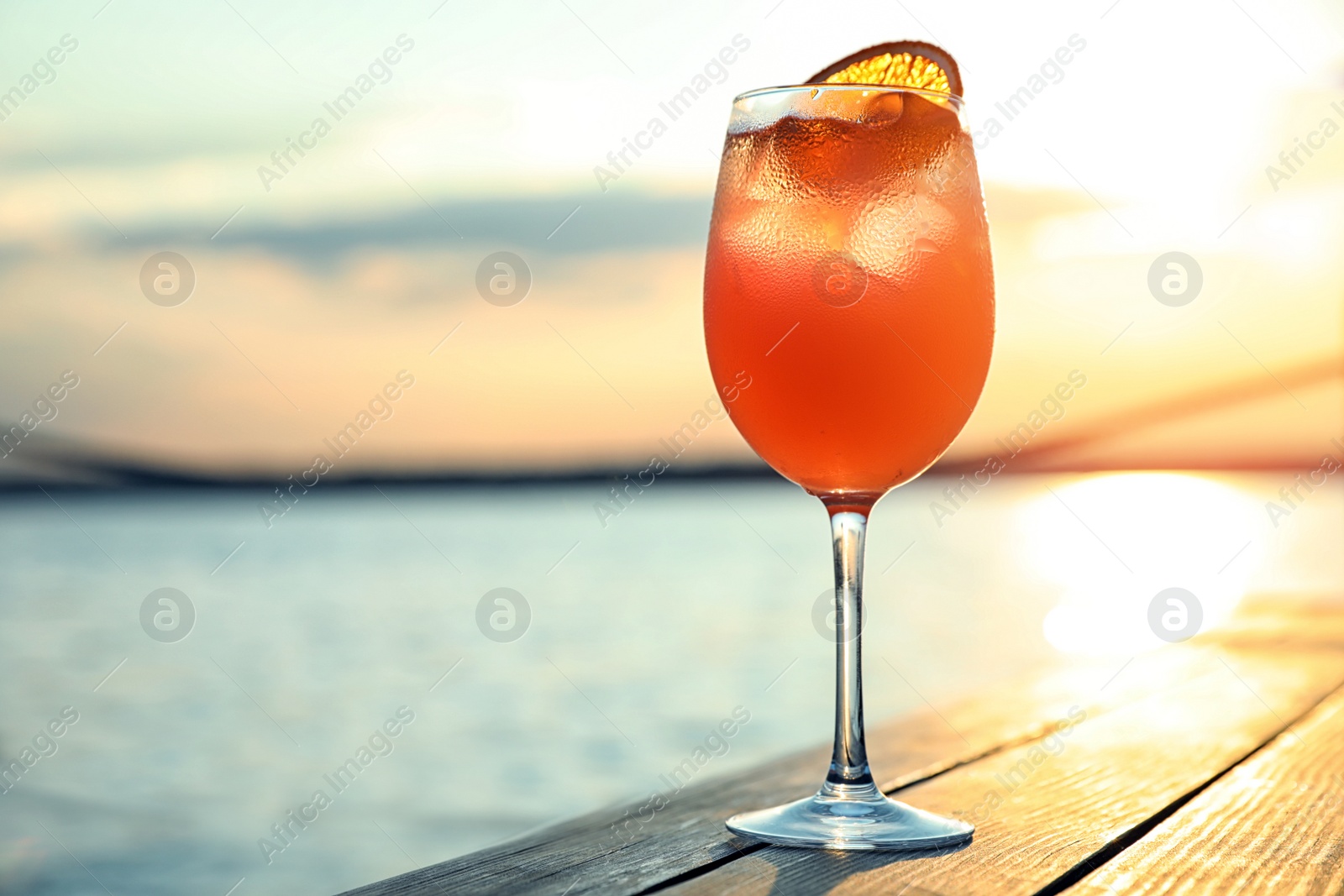 Photo of Glass of fresh summer cocktail on wooden table outdoors at sunset. Space for text