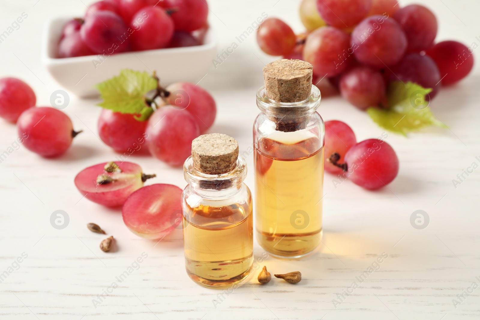 Photo of Organic red grapes, seeds and bottles of natural essential oil on white wooden table